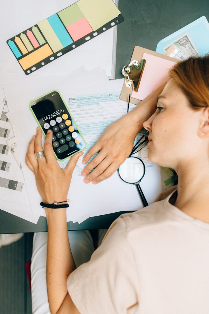 High-angle view of a woman calculating at her desk with documents and office supplies.